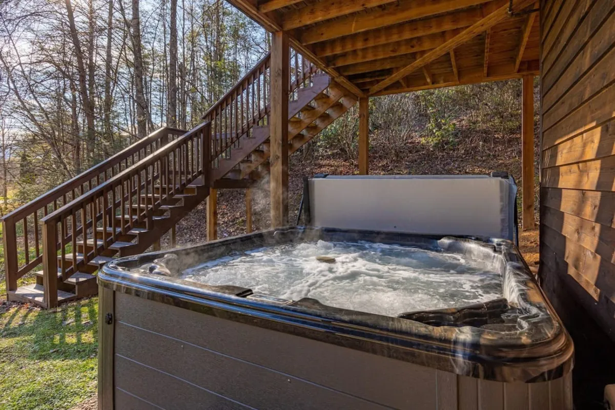 This image displays a tranquil wooden deck nestled among trees, with a bubbling hot tub as the focal point. The scene captures people relaxing in the hot tub, surrounded by the sights and sounds of nature, and hints at shared laughter and bonding moments under the open sky.