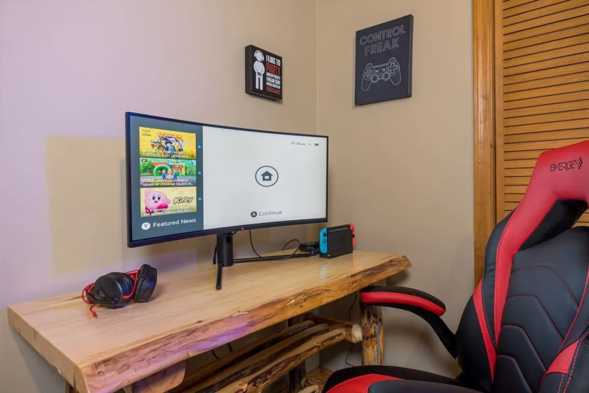 Inside, a vibrant gaming setup features a monitor, gaming chair, Nintendo Switch, and playful wall art. The area exudes energy, providing the perfect space for competitive tournaments or casual gaming sessions with friends.