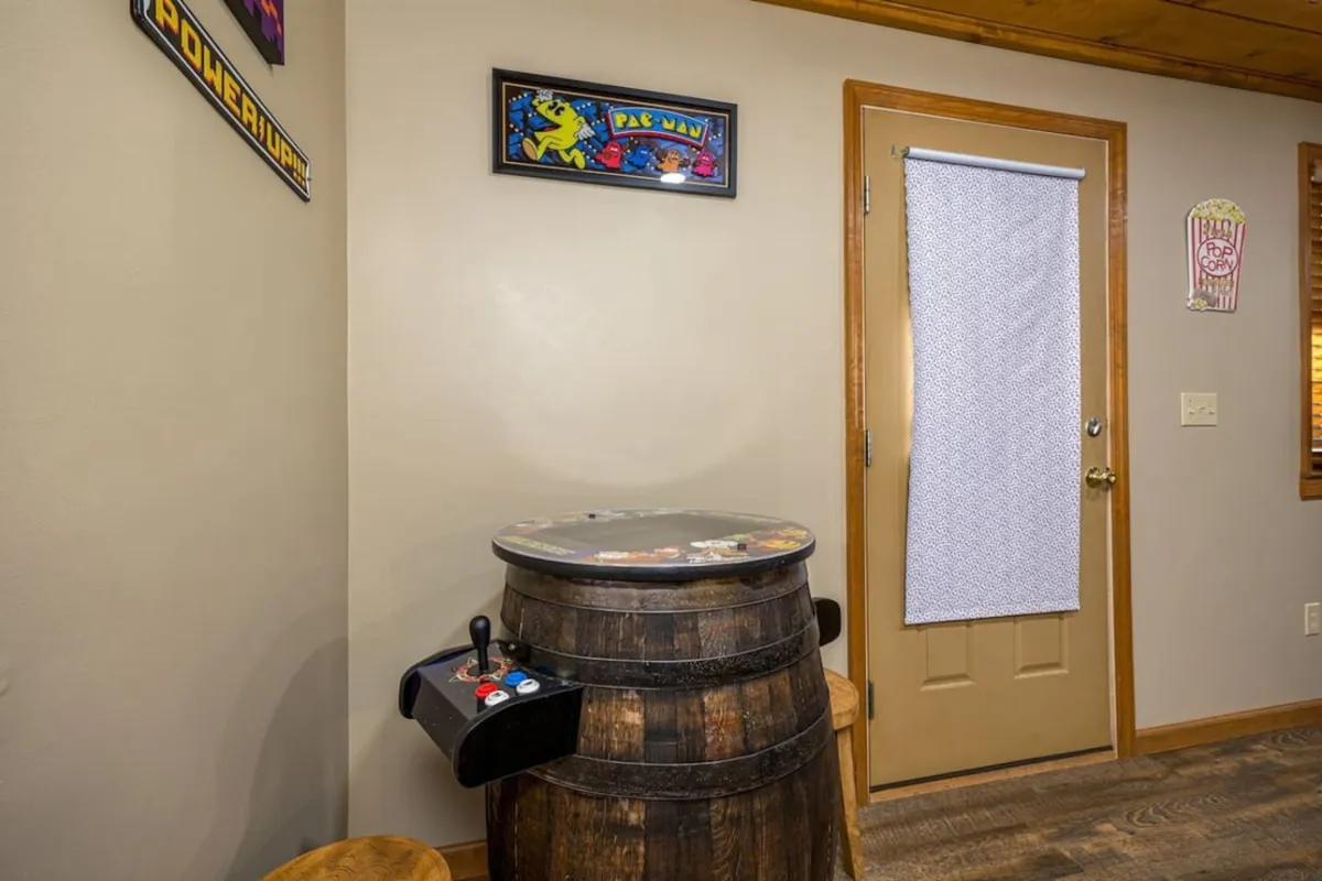 A cozy game room atmosphere highlighted by a barrel arcade game, Pac-Man artwork, and a door with a curtain. The space feels fun and relaxed, evoking nostalgia with classic arcade decor and a playful energy suited for friendly competitions.