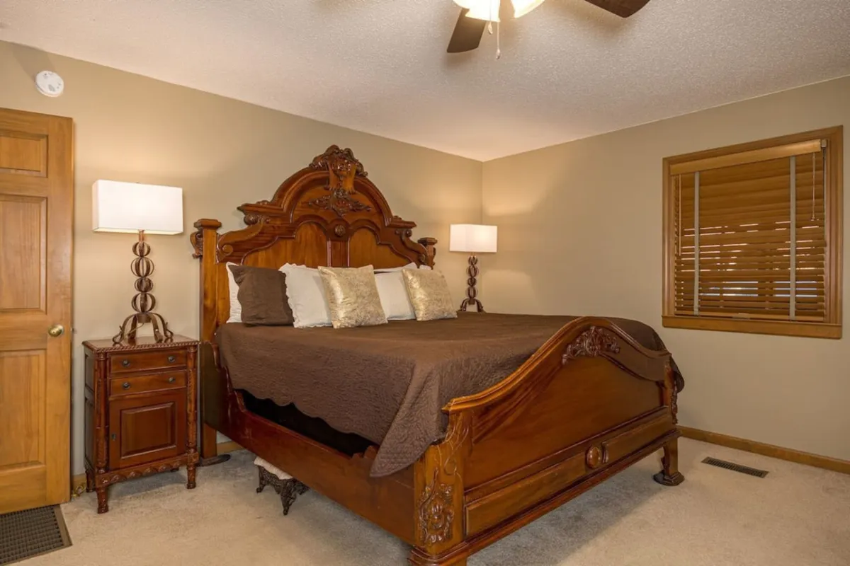 A cozy bedroom featuring an ornate wooden bed with plush bedding, flanked by decorative bedside lamps on a wooden nightstand. The space feels inviting, warm, and perfect for relaxation or a restful night's sleep.