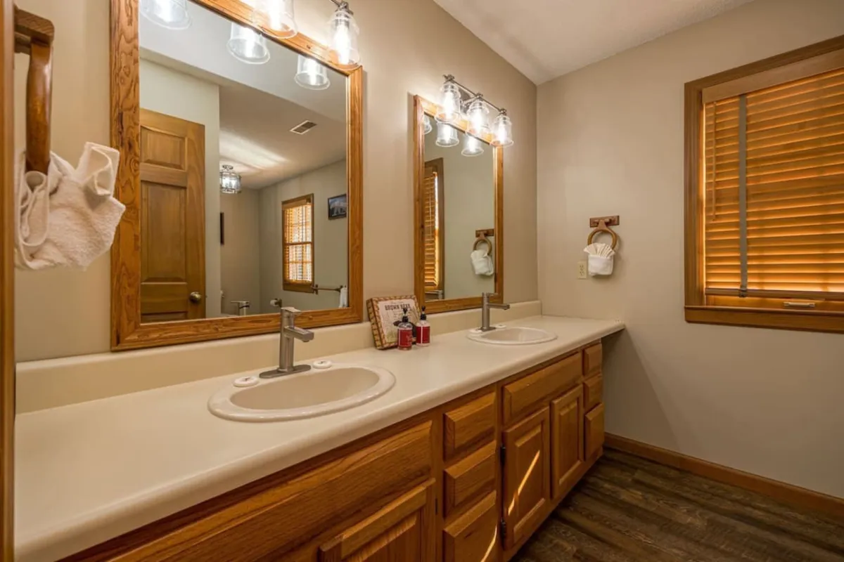 A modern bathroom featuring a double sink vanity with mirrors, wooden cabinetry, and natural light streaming in from a window. The layout is clean and organized, evoking a spa-like sense of calm and refreshment.