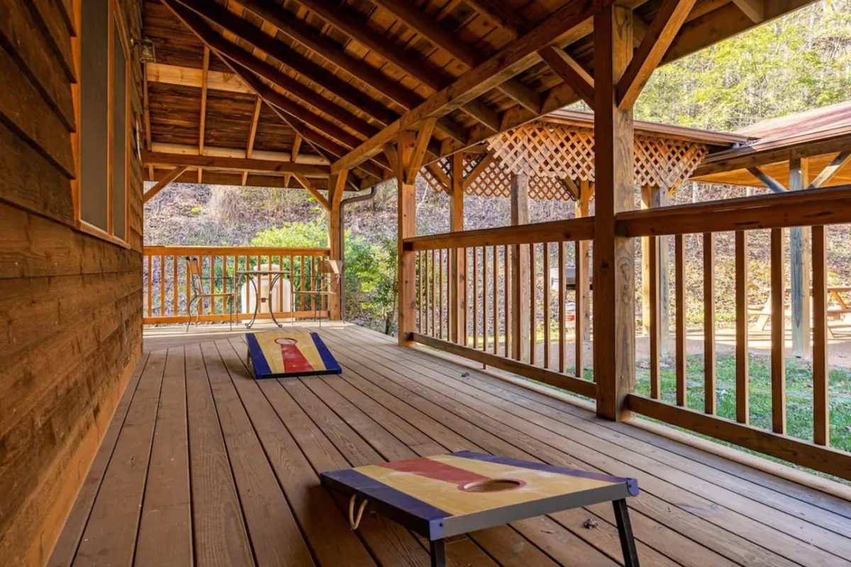 An exterior view featuring bean bag toss game boards set up on a wooden porch with open space beyond, all surrounded by nature. The image radiates playfulness and the spirit of friendly competition.