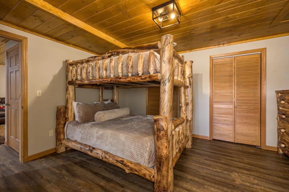 A warm and rustic bedroom with a log bunk bed, textured bedding, and wooden flooring. The space is inviting for families or groups, providing both comfort and a touch of cabin charm.